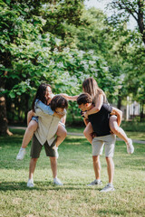 Two young couples enjoying a fun moment together in a lush, green park on a sunny day, sharing...