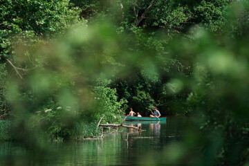 Group in canoe paddling through lush green river surrounded by trees.