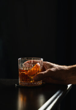 Man's hand holding cocktail in whiskey glass on black background.