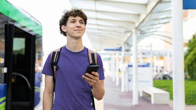 Young Caucasian man with backpack holding smartphone at airport terminal. Concept of travel, waiting, modern lifestyle, and exploring new destinations
