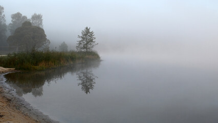 early autumn morning by the lake, fog hides the outlines of trees and bushes, blurred background