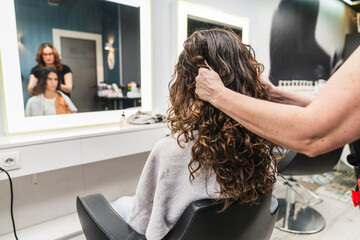 Hair stylist working on a woman's long curly hair in a modern beauty salon, reflecting the process...