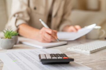 Woman managing home finances, planning family budget, controlling expenses, and working on freelance tasks at the desk with documents, calculator, and notebook