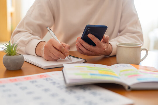 Person is writing in a planner while holding a smartphone, combining analog and digital tools for efficient time management, productivity, and an organized lifestyle - Powered by Adobe