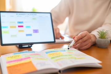 Fototapeta premium Woman managing daily tasks, appointments, and work life balance by highlighting important events in a physical planner and reviewing a digital calendar on a tablet
