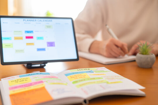 Person organizing daily tasks and appointments for work and home responsibilities using a physical planner and a digital calendar on a tablet for an organized lifestyle