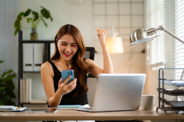 Successful business woman, excited young woman Keeping up arms and showing positive emotions, happy working in modern office on smartphone