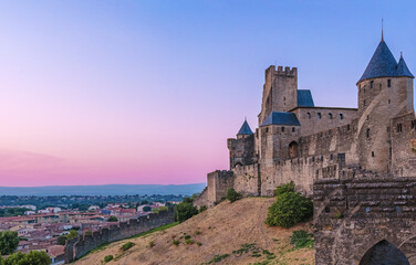 Medieval fortress walls and towers of Carcassonne at sunset, France. Old medieval walls of Carcassonne illuminated by purple sunset sky.