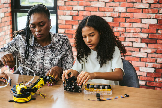 Mentor and student collaborate in classroom lab, assembling robotics kits with sensors and tools. Scene shows diversity, teamwork, research, invention, programming, and teacher-student engagement.