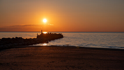 Magical sunset by the sea, old stone pier, the last rays of the sun reflected in the calm sea...