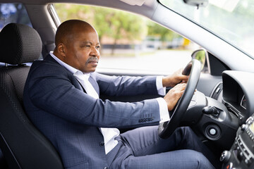 Serious African American businessman sitting in car, honking horn while holding steering wheel with focus, determined expression, confident driver on business trip