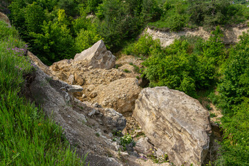 Large boulders scattered across a hillside following a landslide near a lush green forest during the spring season