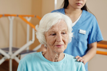 Elderly patient on physical therapy. Senior Caucasian woman looking down thoughtfully while getting...