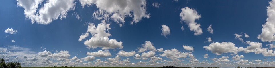 Obraz premium Vast blue sky filled with fluffy white clouds over a green landscape during midday in tranquil countryside