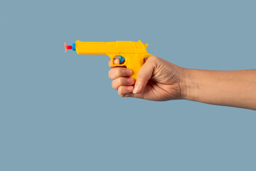 Yellow plastic toy gun in hand on blue background