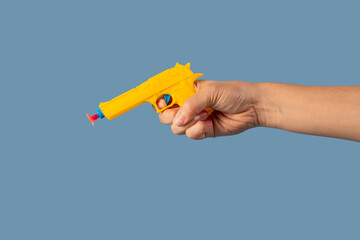 Yellow plastic toy gun in hand on blue background