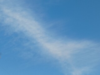 Blue sky with elongated cloud resembling a light trai on a clear day. Minimal natural background.
