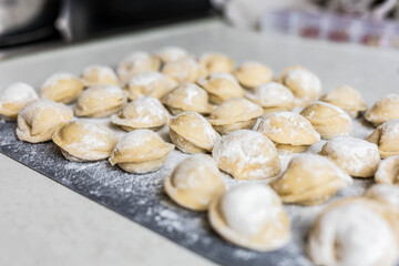 Raw homemade dumplings arranged on a floured board in the kitchen. Traditional cooking process before boiling. Close-up of uncooked pelmeni