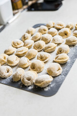 Raw homemade dumplings arranged on a floured board in the kitchen. Traditional cooking process before boiling. Close-up of uncooked pelmeni
