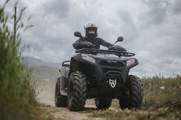 Fototapeta premium Individual wearing protective gear driving an ATV on a dirt track surrounded by nature.