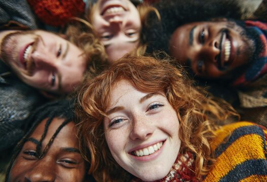Group of diverse friends smiling joyfully while lying on the ground, showcasing happiness and connection, with vibrant sweaters and natural surroundings enhancing the atmosphere