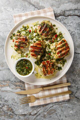 Grilled chicken thighs marinated and drizzled with chimichurri sauce, close-up on a plate on a table. Vertical top view from above
