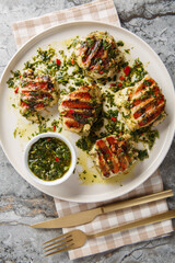 Grilled chicken thighs with Argentinian chimichurri sauce closeup on the plate on the table. Vertical top view from above