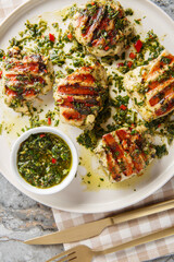 Chimichurri chicken grilled to juicy perfection, and coated in a generous amount of fresh chimichurri sauce closeup on the plate on the table. Vertical top view from above