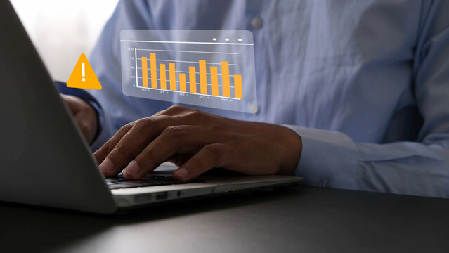 Businessman typing on laptop with warning icon and declining bar chart, indicating data analysis issue or financial risk in digital report, concept of business problem or cybersecurity alert