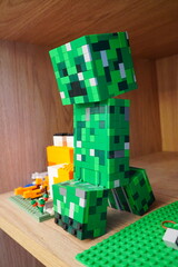 Obraz premium A LEGO model of a Creeper from the popular video game Minecraft displayed on a wooden shelf