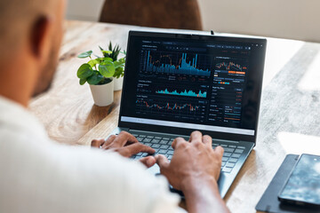 Trader analyzing financial data on laptop at home office workspace
