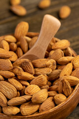 yellow brown whole nuts of unroasted almonds with a wooden spoon on the table, a large number of hard raw almonds on the table during cooking