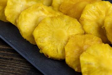 dried ripe bright yellow pineapple fruits on a black slate board, cut into rings and dried yellow clean slices of ripe pineapple for long-term storage and used as a sweet