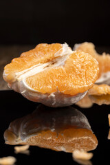 half of an orange citrus on a black mirror surface, ripe sweet and juicy citrus is reflected on the black surface