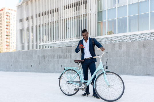 African american entrepreneur using smartphone while holding bicycle outside office