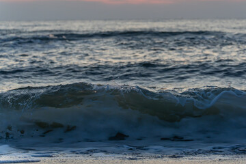 A single wave breaks at dusk. Water droplets glitter in the last light.