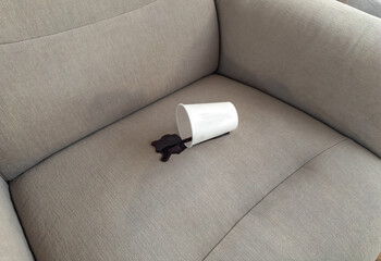 Spilled coffee on beige sofa with white paper cup