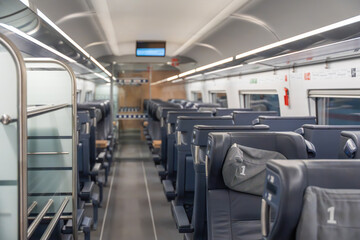First class train interior. First-class train seats in dark leather line the bright carriage. Overhead racks and wide aisles create a spacious travel atmosphere.