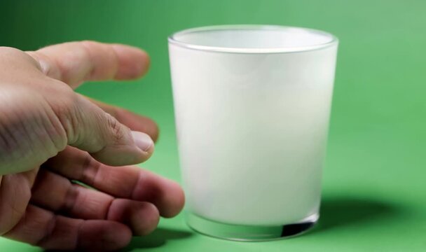 Empty White Glass on Green Background with Hand Reaching for It.