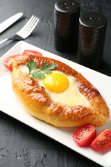Tasty khachapuri with cheese and egg served on black textured table, closeup