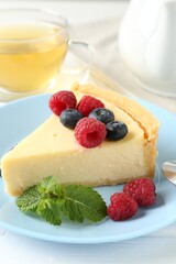Piece of delicious cheesecake with fresh berries and mint served on white wooden table, closeup