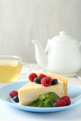 Piece of delicious cheesecake with fresh berries and mint served on white table, closeup
