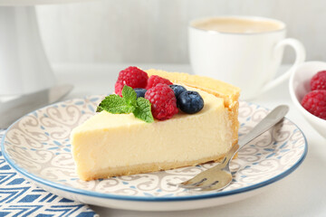 Piece of delicious cheesecake with fresh berries and mint served on white table, closeup