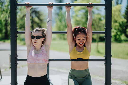 Two women performing fitness exercises on parallel bars at a sunny outdoor park, demonstrating dedication, active lifestyle, and fitness training in a social and motivational setting.