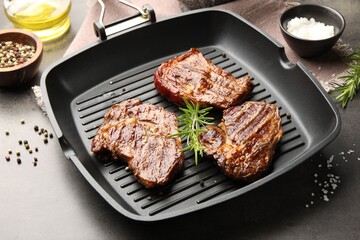 Pan with grilled beef steaks, rosemary and spices on grey textured table, closeup