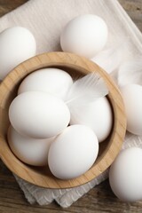 Raw chicken eggs and feathers on wooden table, top view