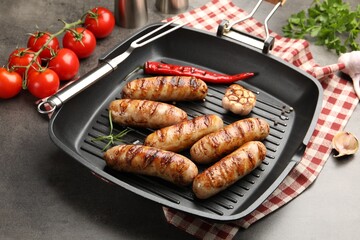 Pan with grilled sausages, spices and tomatoes on gray textured table, closeup