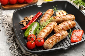 Pan with grilled sausages, vegetables, mushrooms and spices on table, closeup