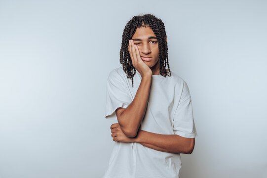 Young person with braided hair in a white shirt looking bored.