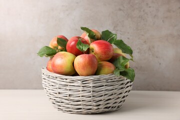 Fresh ripe apples with green leaves in wicker basket on white wooden table